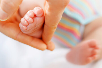 Father or mother holding foot of newborn baby. Adult hand and baby tiny baby feet. Happy parenthood, carefree childhood, family, love, tenderness