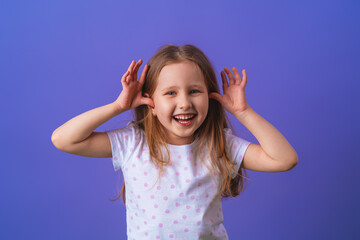 Little girl 5 years old with blonde hair in a T-shirt with colored polka dots standing happily smiling on purple background. Close-up. the model is having fun and feels overwhelmed, amazed.