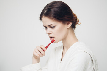 morning procedures woman brushes teeth on a light background and a white robe