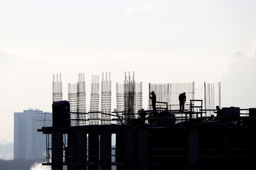 Silhouettes of workers on construction site against the sky. Housing construction, builders working on scaffolding of unfinished building