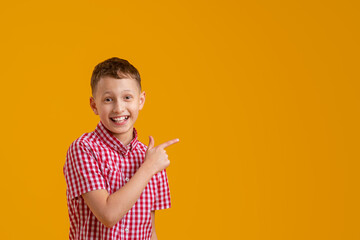 cheerful, happy child points up, copying the place for the text. A smiling, enthusiastic teenage boy in a plaid shirt shows off. Advertising concept.