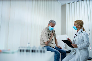 An elderly man not feeling well while doctor writing down symptoms during COVID-19 pandemic.