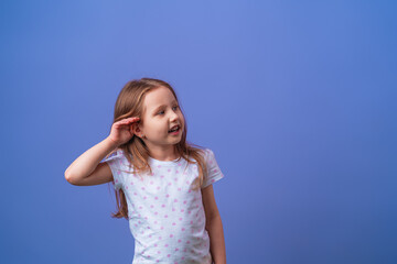 charming little girl smiles with her hand over her ear while listening and hearing rumors or gossip...