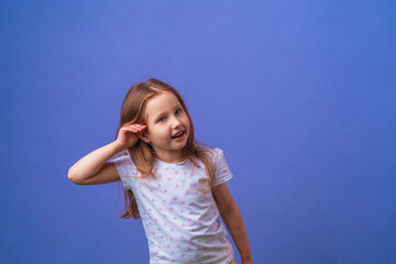 charming little girl smiles with her hand over her ear while listening and hearing rumors or gossip...