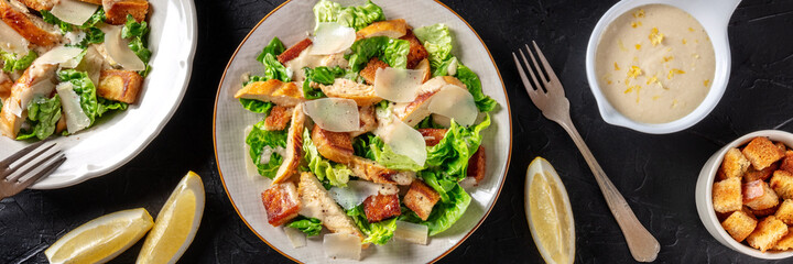 Caesar salad panorama on a dark background. The classic salad with chicken and Parmesan, a flat lay, shot from the top