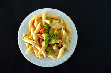 Pasta with vegetables and cheese, top view, black background, penne 