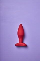 small red butt plug, sex toy for adult, designed anal plug isolated on purple background. minimal...