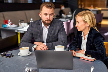 two business colleagues discussing project using laptop, theysit in restaurant talking, co-working