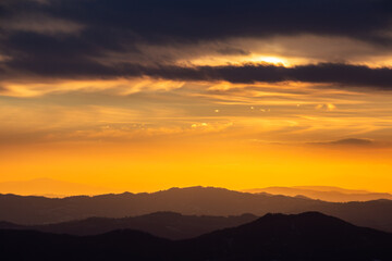 Sunset with sun hidden behind clouds over mountains and valley