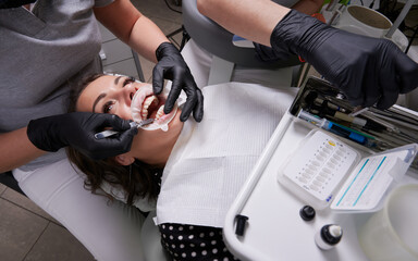 Woman patient in dental chair during procedure of installing braces to teeth. Dentist and assistant...