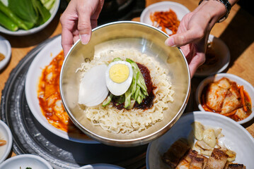 Korean cold noodles. A bowl of noodles with red spicy sauce, topped with slice vegetabled, boiled egg and ice.