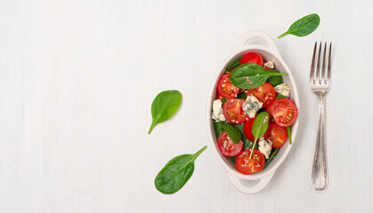 Cherry tomato salad with spinach and blue cheese on white background.