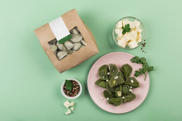 Green spinach dumplings with cheese in eco-friendly paper packaging for delivery and on a pink plate on a green background.