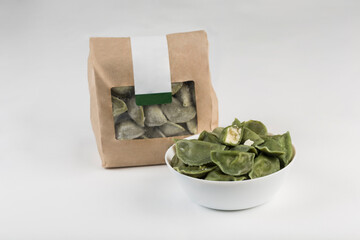 Green spinach dumplings with cheese in a bowl and eco-friendly paper packaging for delivery on a white background, isolated.