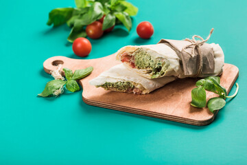 Falafel roll of pita bread with hummus, fresh basil and cherry tomatoes on a wooden board on a green background.