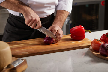 Unrecognizable cook cutting onion on wooden board, making Salad concept. Knife cuts purple onion. Professional chef prepares vegetables for soup. Cooking of vegetarian dish.