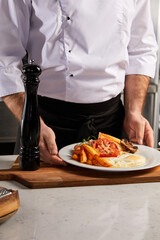 cropped chef representing english breakfast on plate, showing at camera cooked meal, putting on wooden board