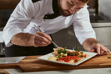 Cook man neatly decorates the dish. young professional chef adding some piquancy to meal. in modern kitchen, at work in uniform