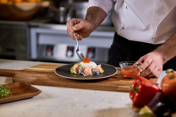 professional cook adds red caviar for salad, making tasty food in restaurant, master class of cooking. close-up photo