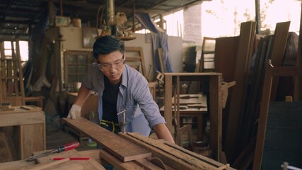 Professional asian carpenter working on wood craft in workshop to produce wooden furniture during the day. DIY maker and carpentry work concept.