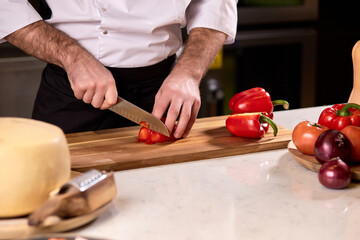 Obraz na płótnie Canvas close up of male hand cutting pepper on cutting board in restaurant kitchen. cooking, food and restaurant concept