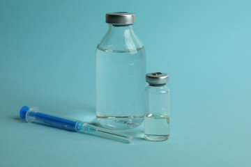 Vials with Covid - 19 vaccine and syringe on blue background