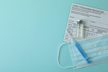 Vaccination record card, mask and syringe on blue background