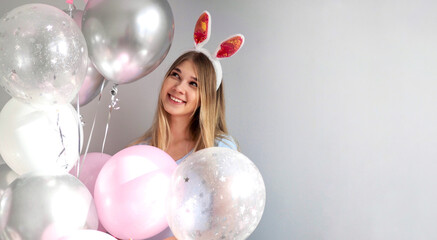 Happy girl in costume bunny with ears. Girl in rabbit costume having fun with pink balloons. Happy easter banner. Young smiling woman wearing bunny ears on Easter day. Easter Bunnies. Copy space