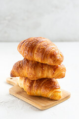 Croissants in a stack on a wooden board on a white background. 