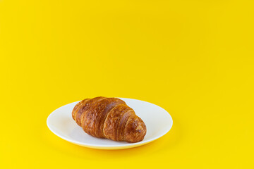 Croissant on a white plate on a yellow background.