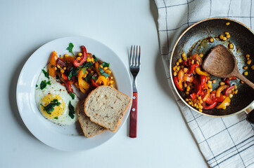 tasty vegetarian farm style breakfast - fried egg with baked sweet peppers and corn with parsley and whole grain bread served on white plate