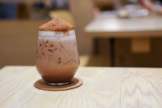 Iced Chocolate Bomb topped with cocoa powder likes volcano on wooden table in cafe.