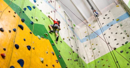 Fotobehang Sporty little girl climbing artificial boulder on practical wall in gym © Angelov