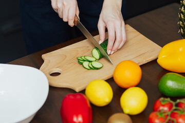 Cropped shot of woman is preparing vegetable salad in the kitchen. She cutting ingredients on cutting board. Healthy food. 