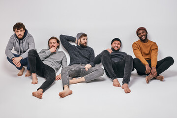 smiling men sit on floor having fun, talking, wearing stylish casual outfits, cheerful guys in studio on white background. fashion, people concept