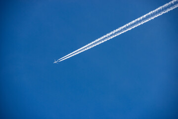 A white Airliner with contrails flying in a clear blue sky, seen directly below, photography.