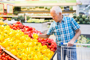 elderly retired man buying bell pepper in grocery section of supermarket
