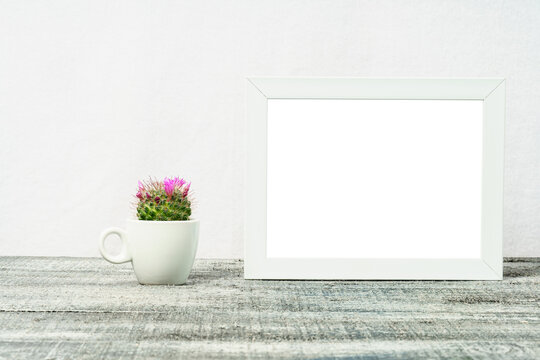 Mock up of a white frame with a cactus on a black table. Empty photo frame and blooming cactus in a white cup.