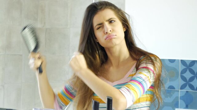 Woman in front of mirror in the morning trying to brush long messy hair fighting