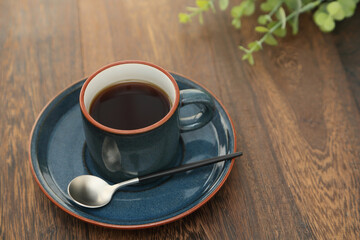 Coffee in a blue cup on a wooden table. With a modern coffee spoon and eucalyptus leaves.