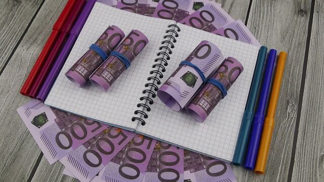 Financial, wealth or business concept with rolls of 500 Euro bills on an open blank notebook placed over fanned banknotes on a stone counter. Rotating table