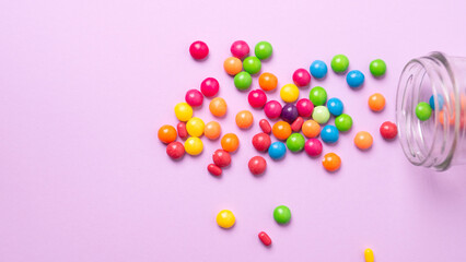 colorful candies poured from a glass jar on a colored background