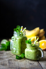 Two healthy green smoothies with spinach, banana, orange and mint in glass jar and ingredients. Detox, diet, healthy, vegetarian food concept. Copy space
