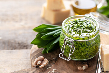 Wild leek pesto with olive oil and parmesan cheese in a glass jar on a wooden table. Useful...