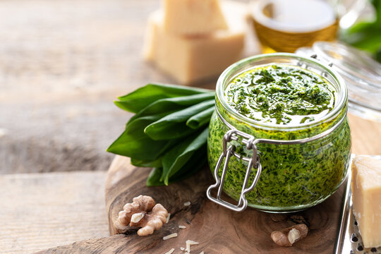 Wild leek pesto with olive oil and parmesan cheese in a glass jar on a wooden table. Useful properties of ramson. Leaves of fresh ramson. Copy space
