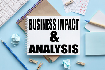 BUSINESS IMPACT ANALYSIS, business concept. text on white notepad paper on blue background. near the blue sticks and a white keyboard