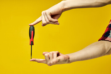 Black and red screwdriver isolated on yellow background, cropped male holding instrument tools in...