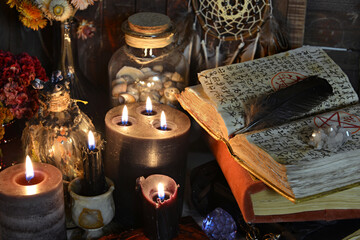 Open grimoire book of spells, burning candles, runes and ritual objects on witch table.