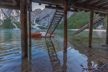 Rowing boats moored near a wooden stair in an idyllic setting with mountain reflections and a small church, Braies Lake, South Tyrol, Italy. Concept: relaxation in nature, famous natural places