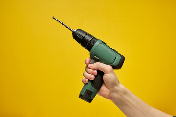 Green cordless battery powered drill on yellow background, cropped male hands holding tool for...